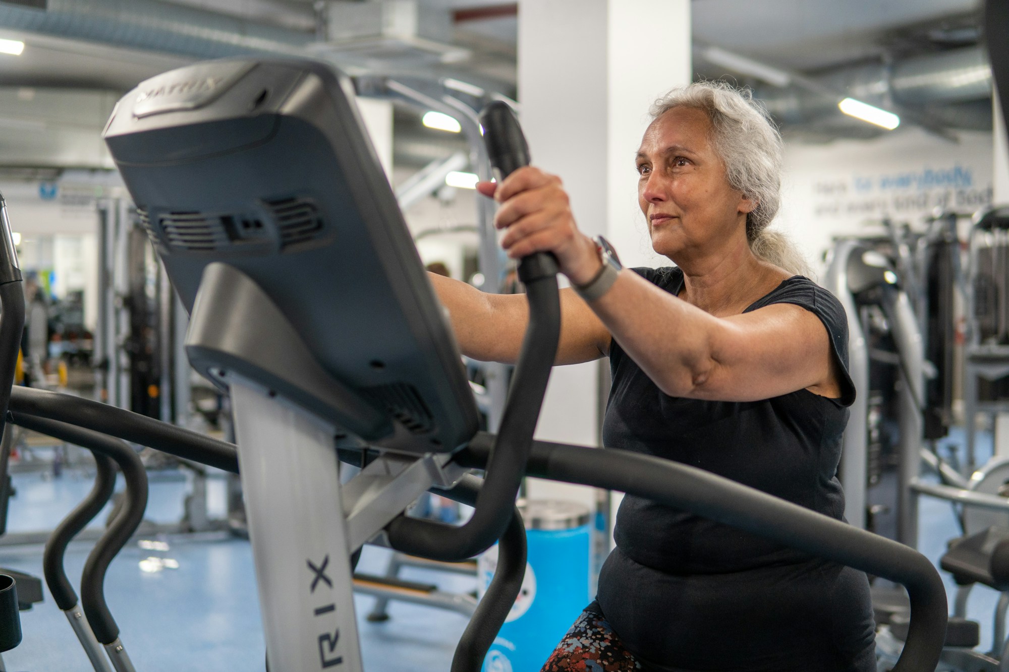 Senhora de cabelo grisalho pedalando num aparelho de cardio, concentrada